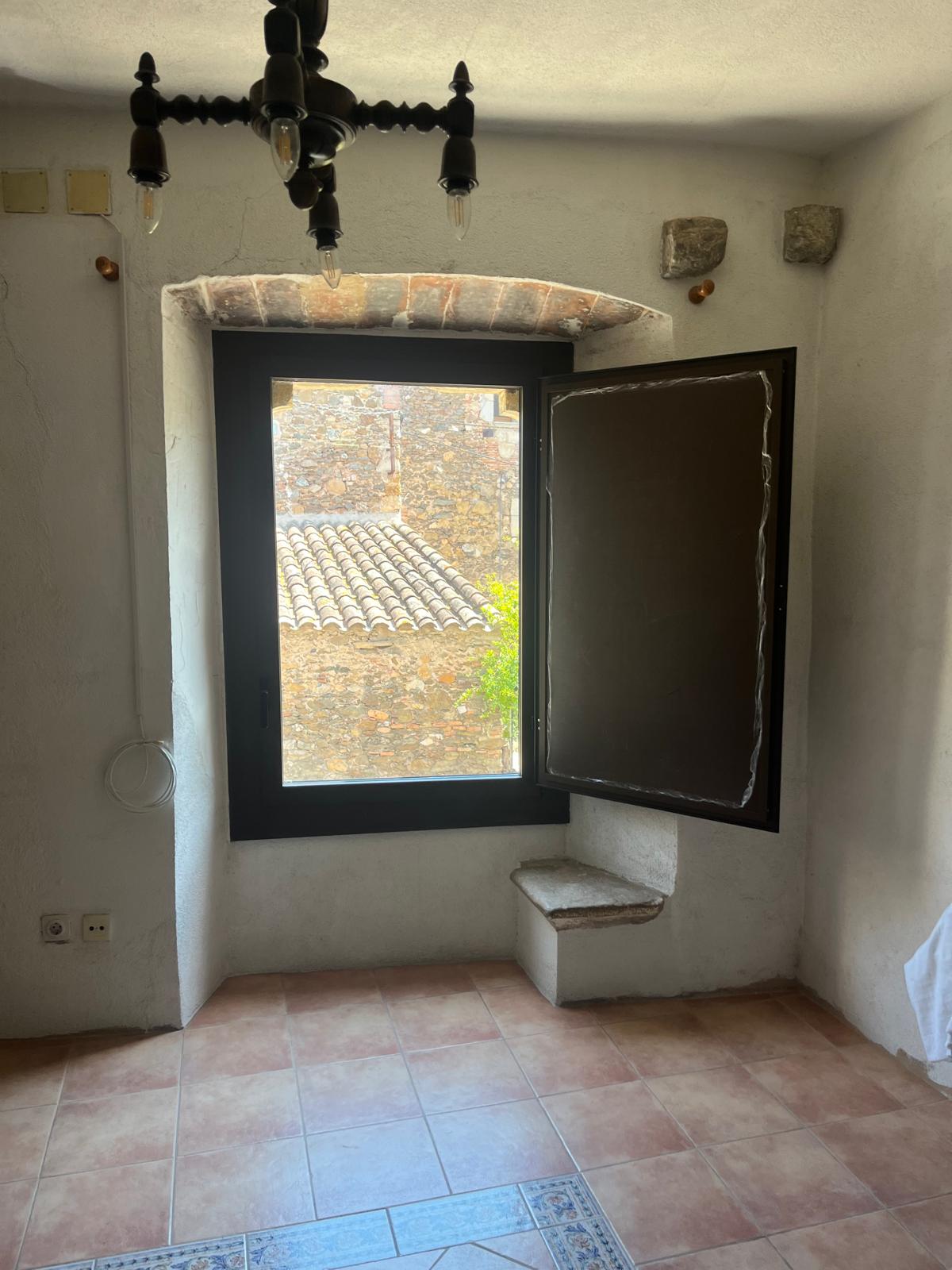 Ventana de marco oscuro con contraventana interior abierta en Celrà